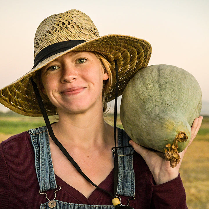 Baker Creek Manager holding a Sibley or Pikes Peak Winter Squash on her shoulder in the field.