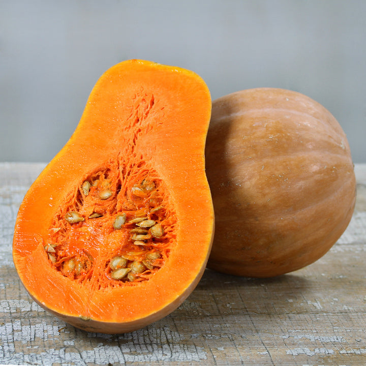 Sucrine Du Berry Winter Squash cut open to show the orange flesh on wooden table.