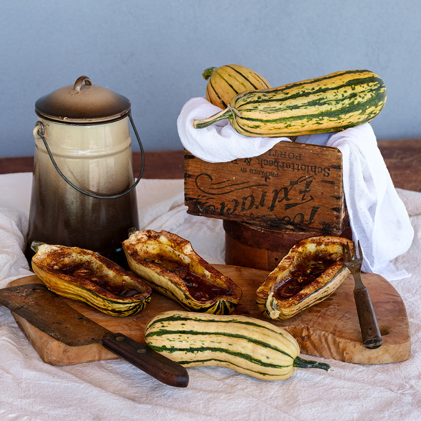 Bakes and whole fresh Delicata Winter Squash on a wooden cutting board with utensils.