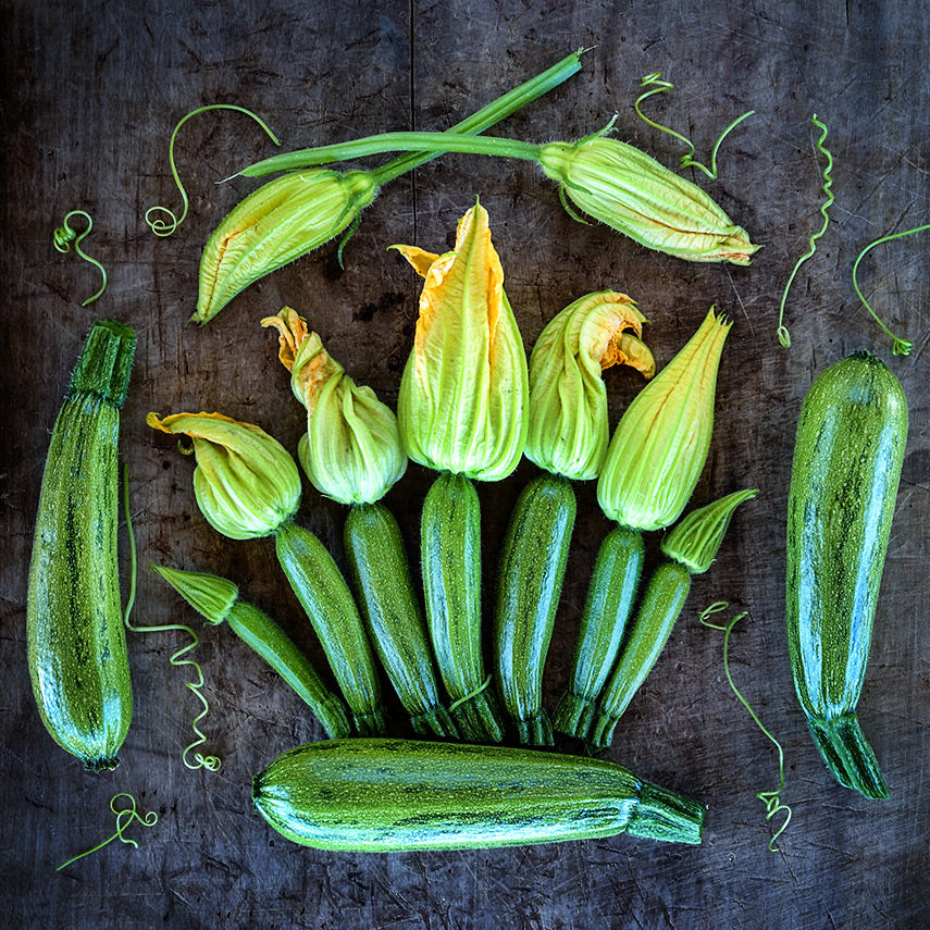 Caserta Summer Squash with blooms and curly stems on wooden cutting board.
