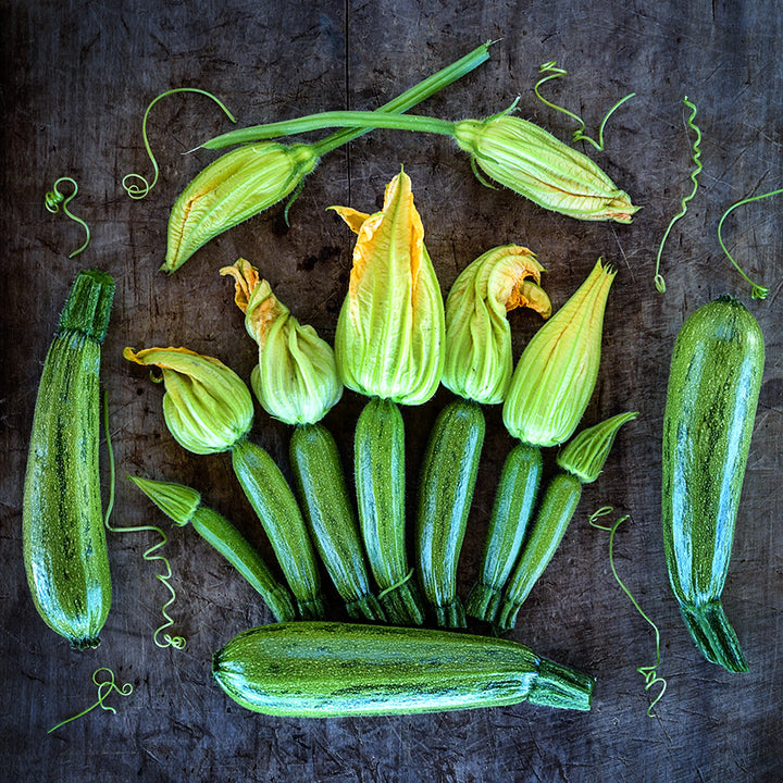 Caserta Summer Squash with blooms and curly stems on wooden cutting board.