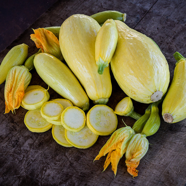 Cut and whole Early Prolific Straightneck Summer Squash arranged on wooden with blooms.