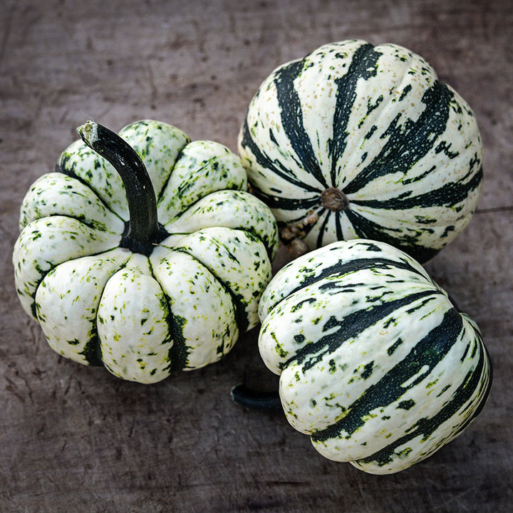 Three Sweet Dumpling Winter Squash on a wooden cutting board.
