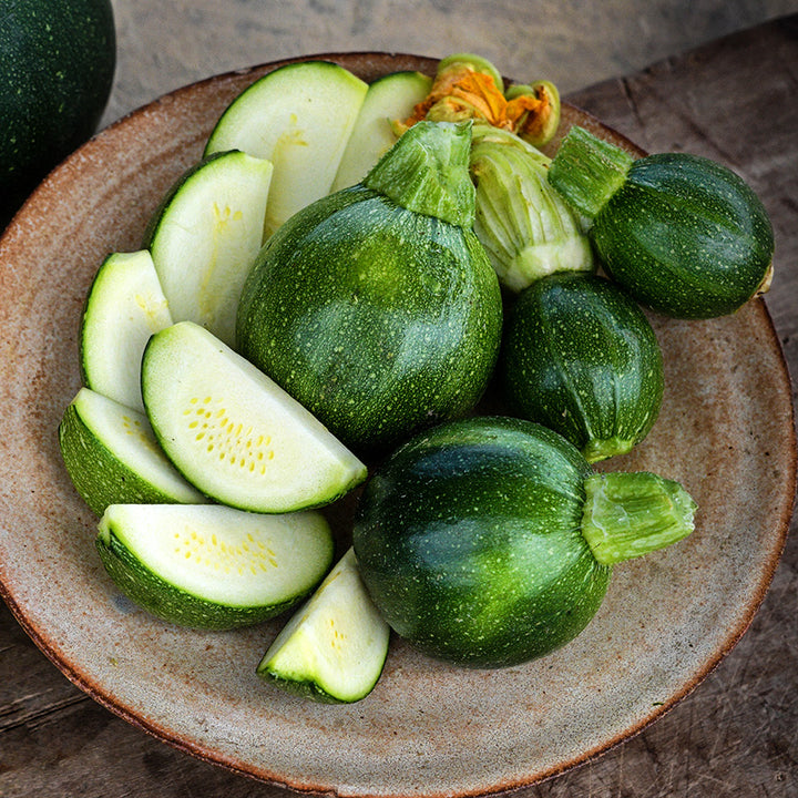 Young sliced and whole Tondo Scuro Di Piacenza Summer Squash on a ceramic plate.
