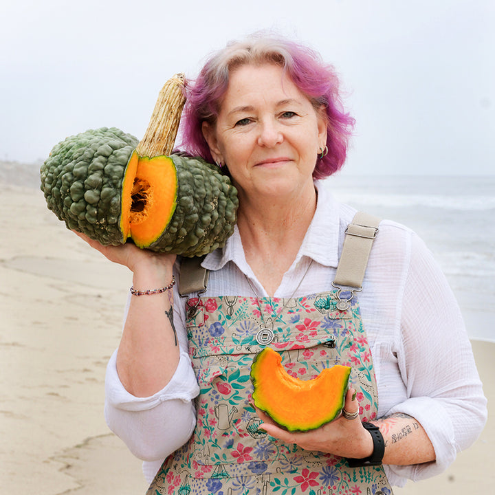 A Baker Creek manager smile while holding cut open Marina Di Chioggia Pumpkin on the beach.