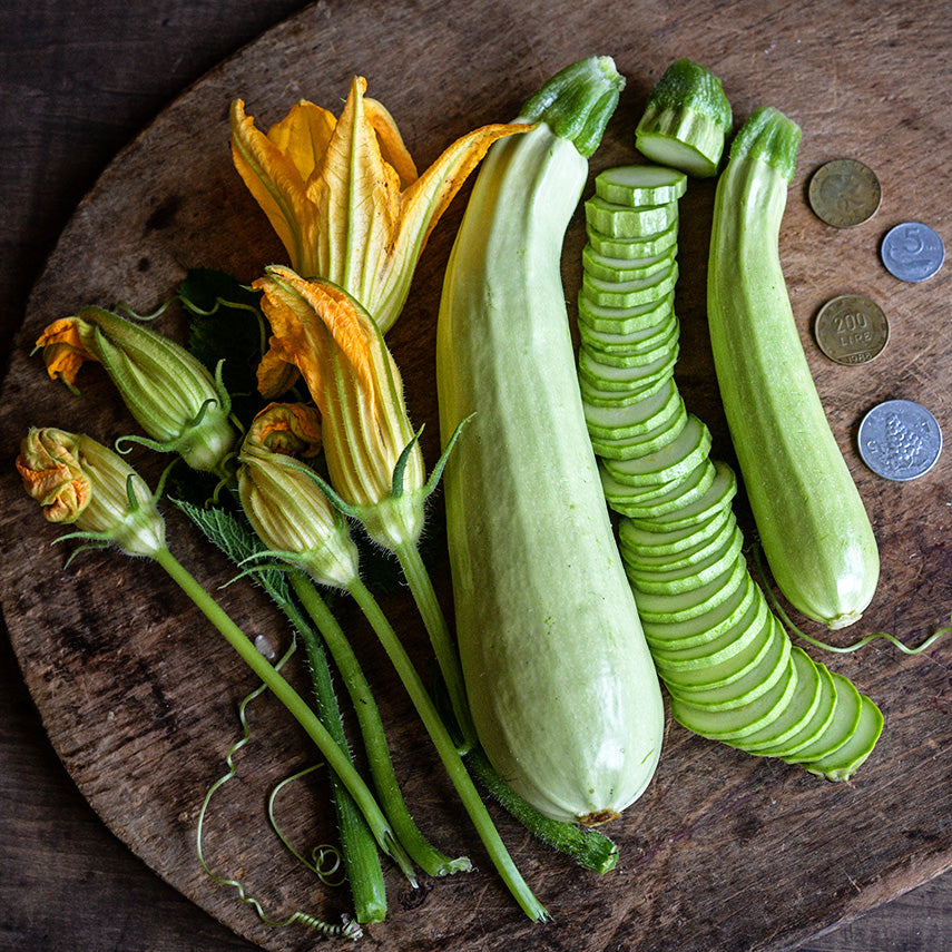 Long White of Palermo Zucchini Summer Squash sliced and whole with blooms on a wood background.