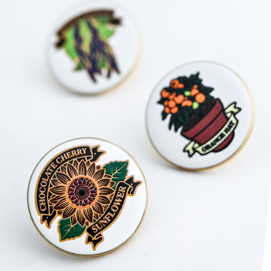 A trio of Limited Edition Pins with the Chocolate Cherry Sunflower Limited Edition Pin shown in the foreground.