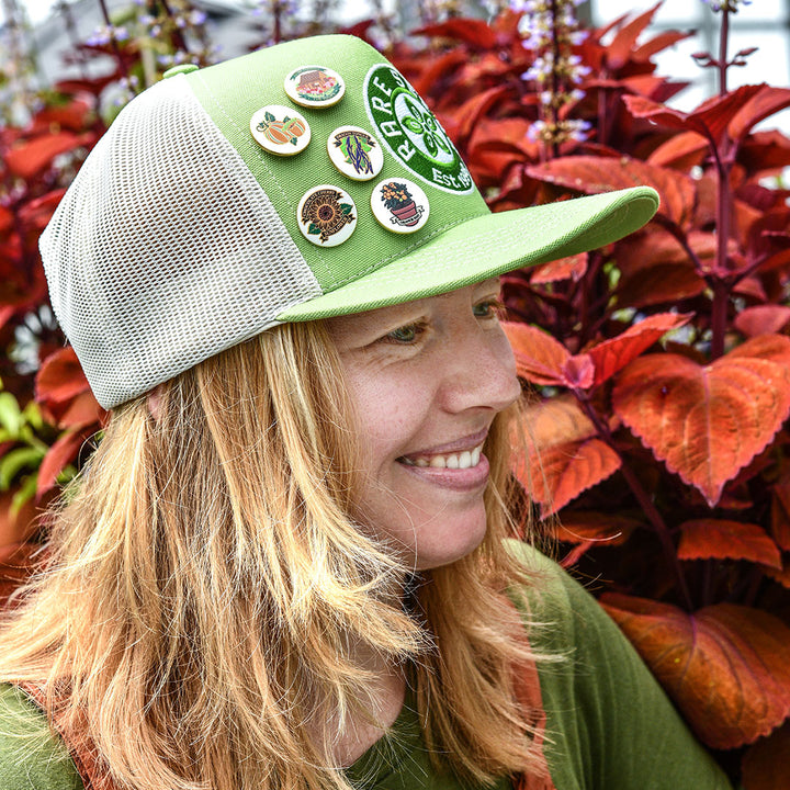 A Baker Creek employee is shown wearing Chocolate Cherry Sunflower Limited Edition Pin on a hat.