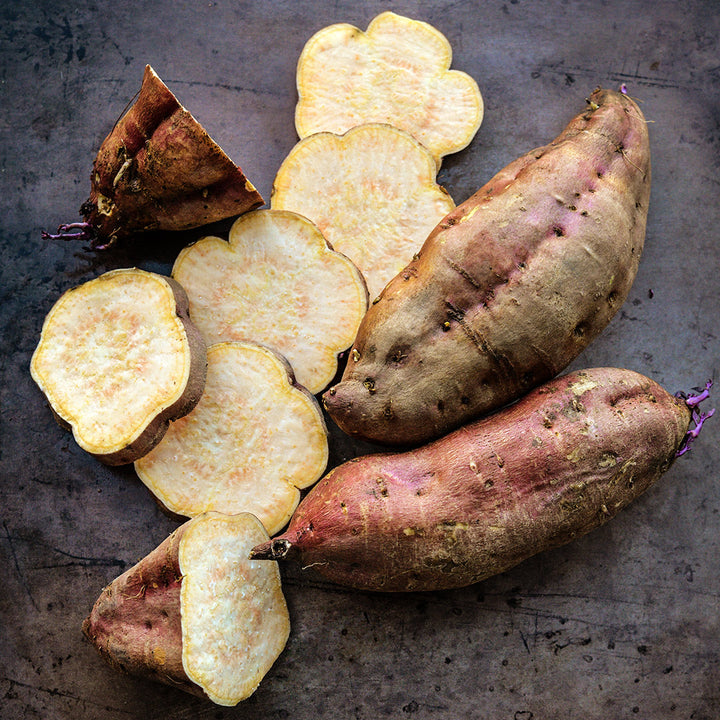 Cut and whole Korean Gold Sweet Potatoes on a brown background.