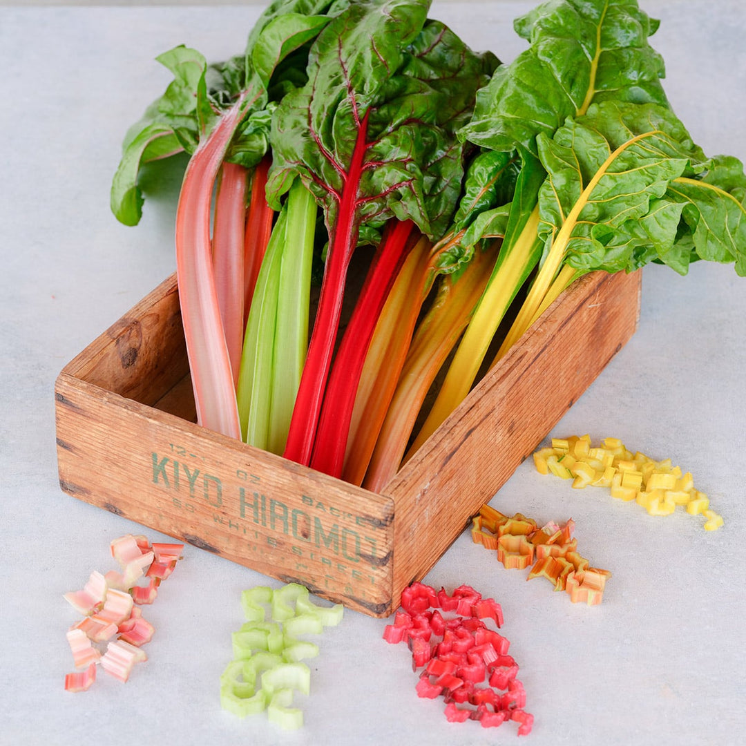 Five Color Silverbeet Swiss Chard in a wooden box surrounded by chopped stems on a light background.
