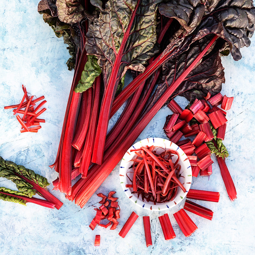 Overhead view of whole and chopped Vulcan Swiss Chard on light blue background.