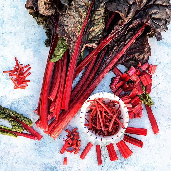 Overhead view of whole and chopped Vulcan Swiss Chard on light blue background.