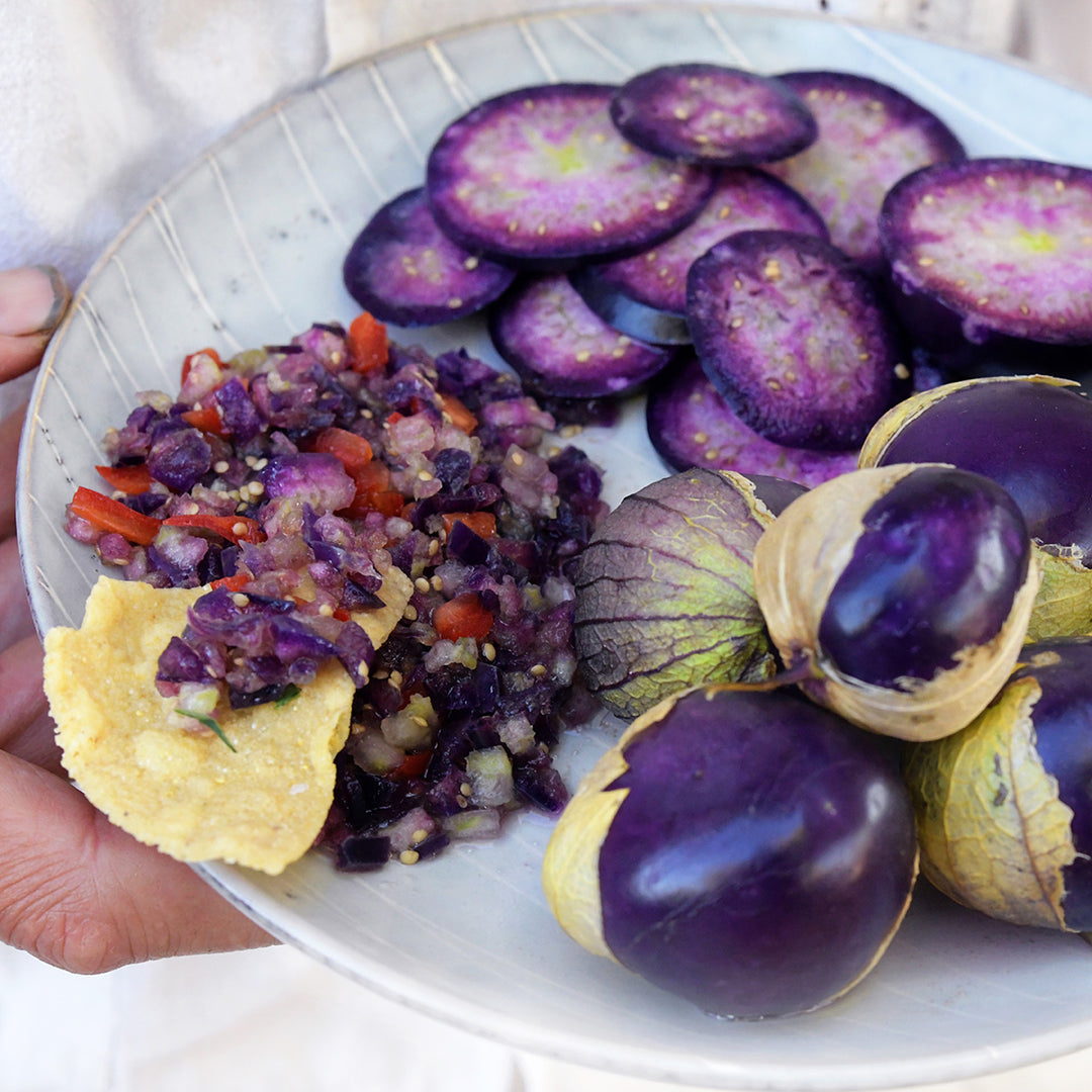 Hand holding a plate of whole, sliced Purple Tomatillos with a side of purple salsa.