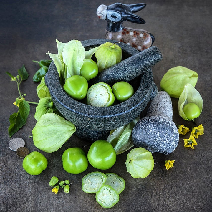 Rio Grande Verde Tomatillos in and around a mortar and pestle on a dark background.