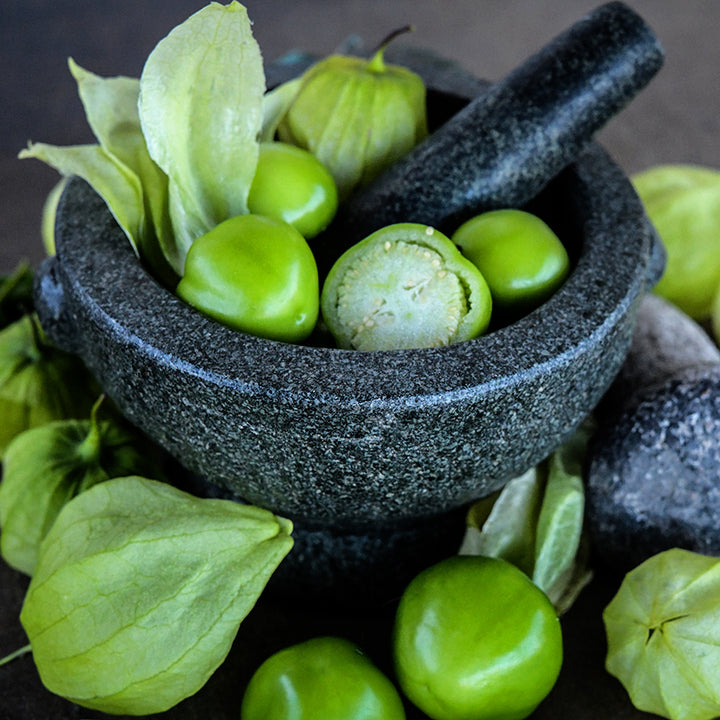Rio Grande Verde Tomatillos in a mortar with a pestle to make salsa.