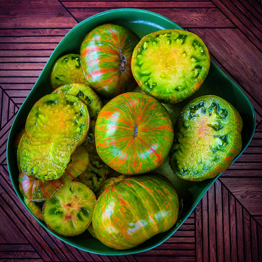Whole and cut Berkeley Tie-Dye Green Tomatoes on a green plate on a parkay wood background.