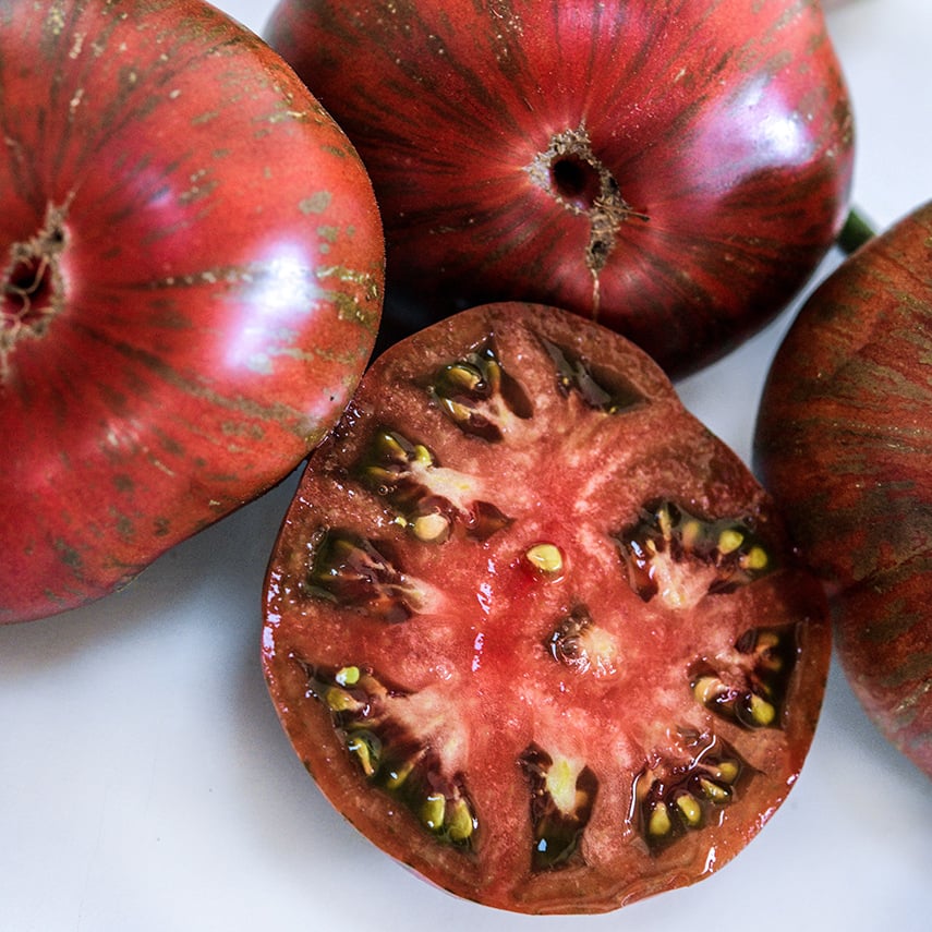 Cut and whole Berkeley Pink Tie-Dye Tomatoes on a white background.