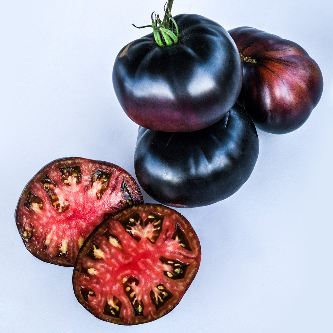 Three whole stacked Black Beauty Tomatoes with a couple of slices on white background.
