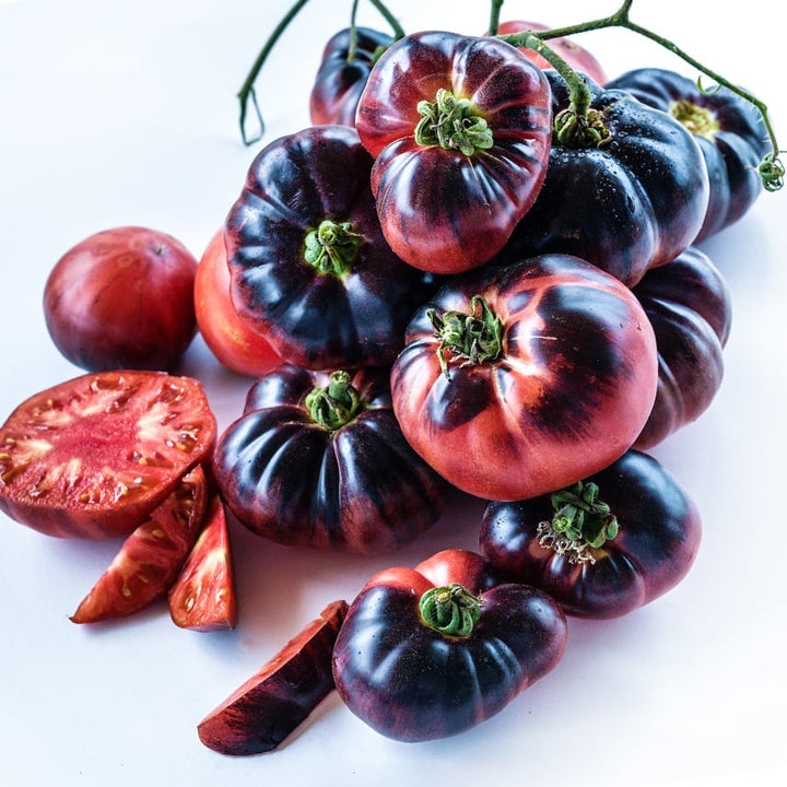 A cluster of whole and cut Blue Beauty Tomatoes on a white background.