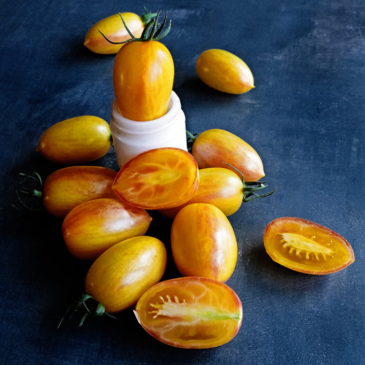 Cut and whole Tiger Blush Tomatoes arranged on dark blue background.