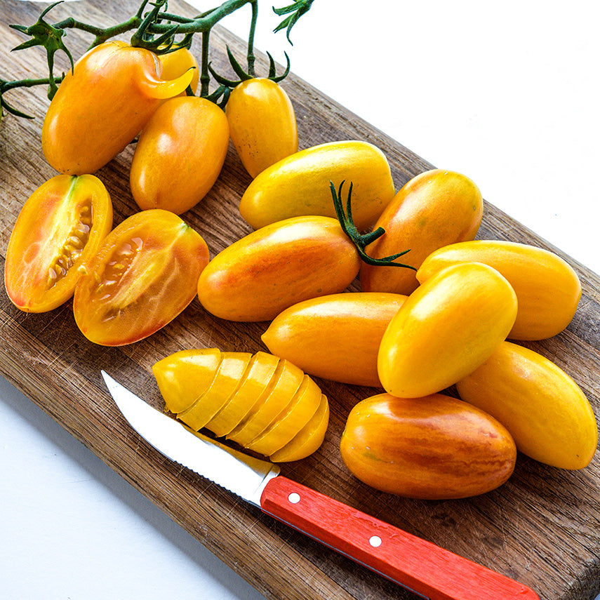 Tiger Blush Tomatoes arranged on wooden cutting board with an orange handled knife.