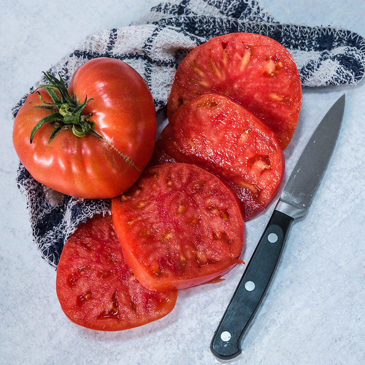A Brandywine Sudduth's Strain Tomato with four slices on dish towel with a knife.