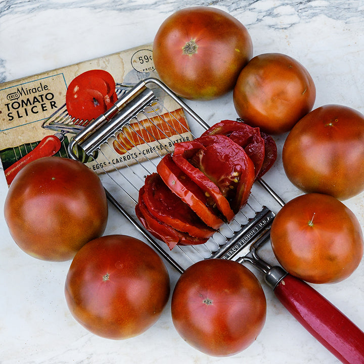 Brown Sugar Tomatoes with a tomato slicer surrounded by whole tomatoes on a white marble background.
