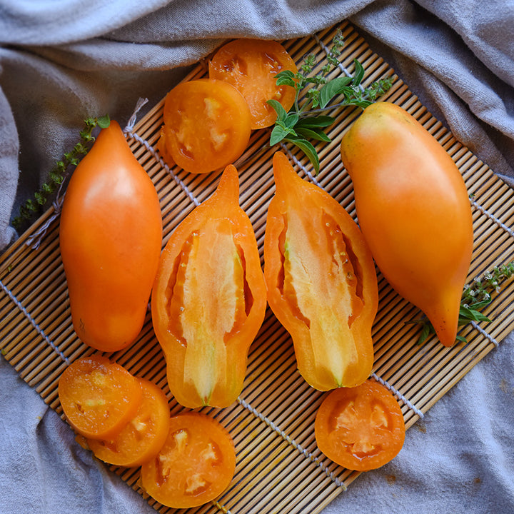 Buratino or Pinocchio Tomatoes sliced and whole on a bamboo mat with basil leaves.