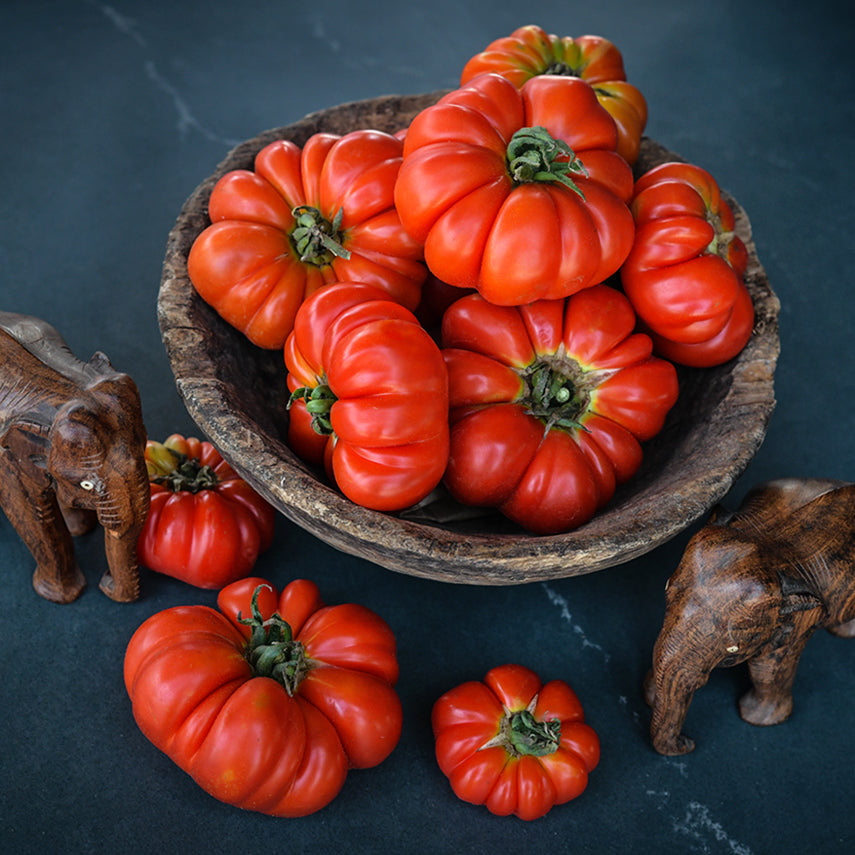 A wooden bowl full of Burmese Sour Tomatoes with wooden elephants on a jade background.