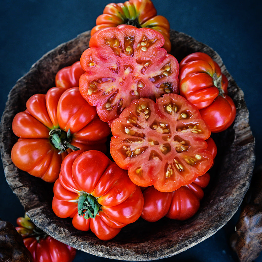 Cut and whole Burmese Sour Tomatoes in a rustic wooden bowl on a dark jade background.