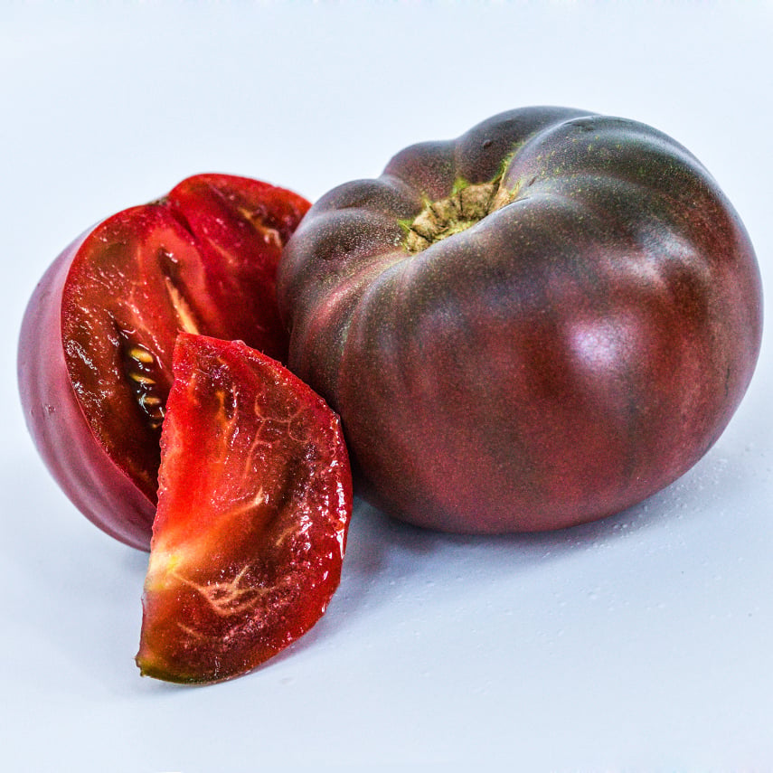 One whole Cherokee Purple Tomato with a slices on a white background.
