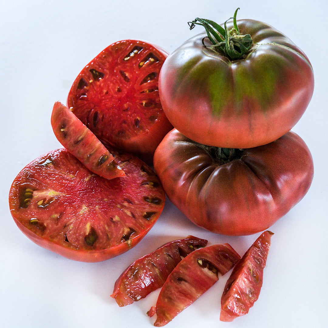 Stacked whole and cut Chocolate Miracle Tomatoes resting on a white background.