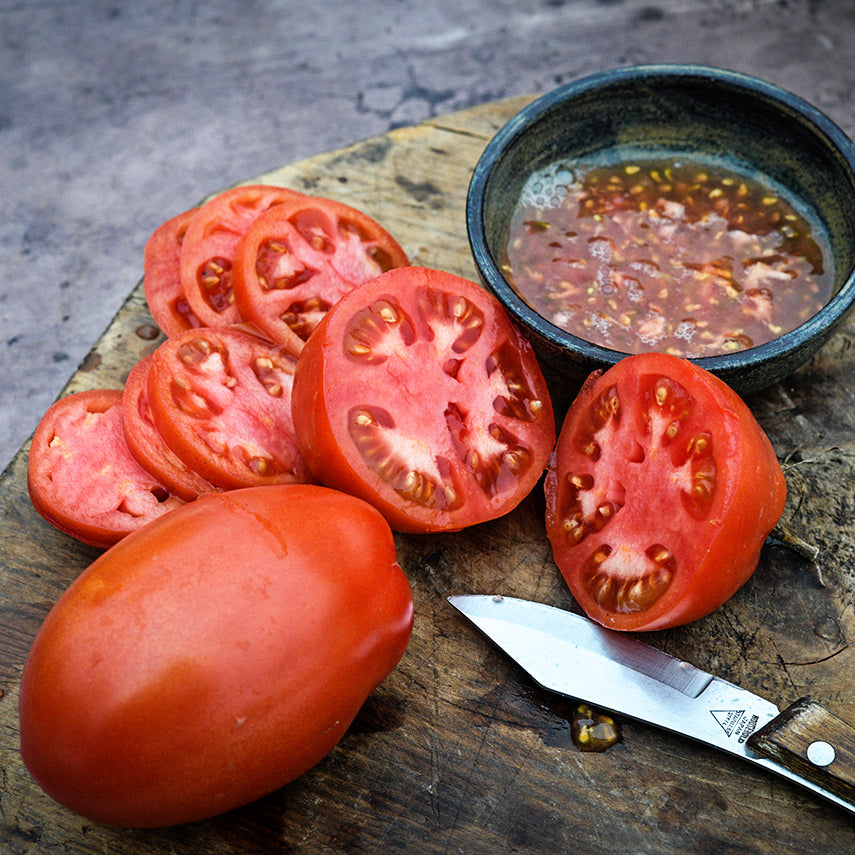 Sliced and juiced Comstock Sauce and Slice Tomato on a wood cutting board with a wood handled knife.
