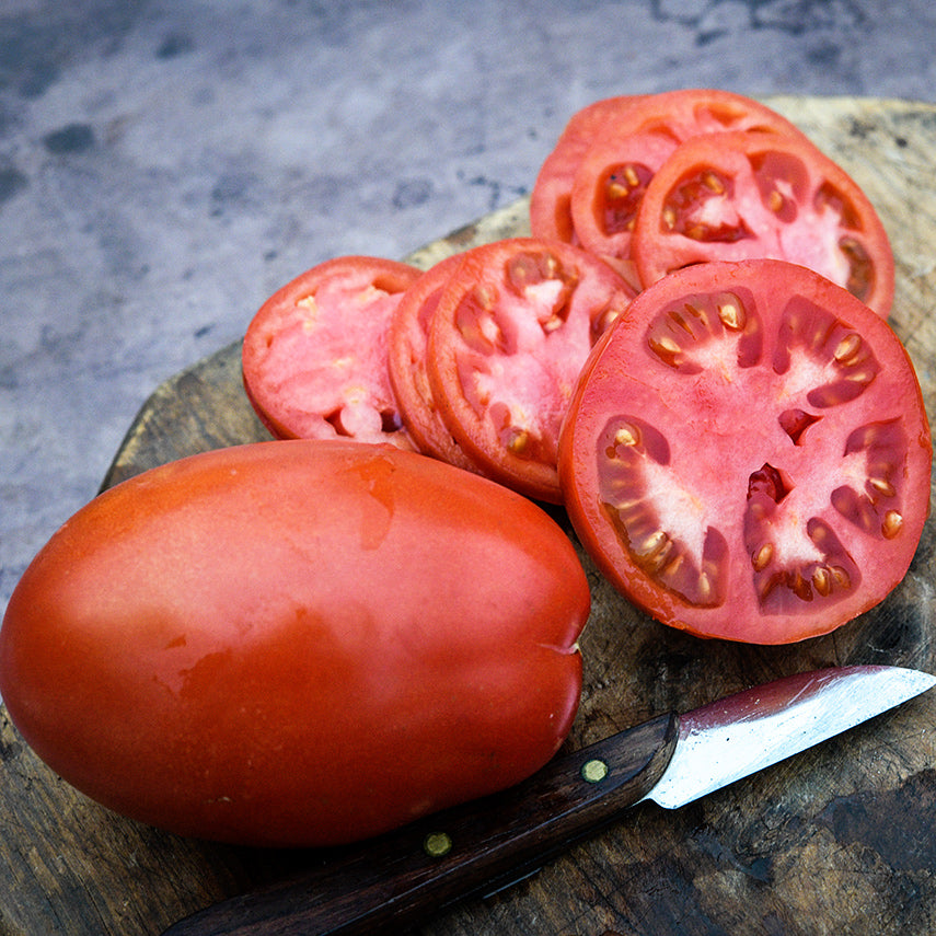 Close-up of a whole Comstock Sauce and Slice Tomato with slices and knife on wood cutting board.