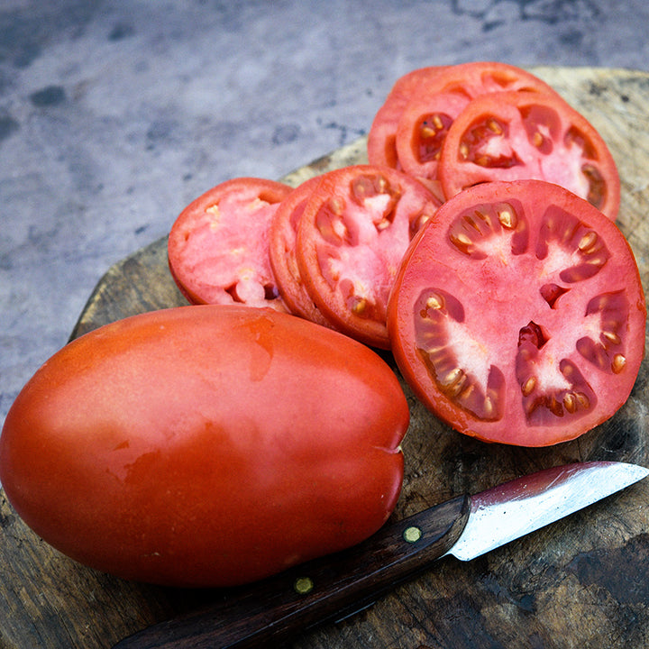 Close-up of a whole Comstock Sauce and Slice Tomato with slices and knife on wood cutting board.