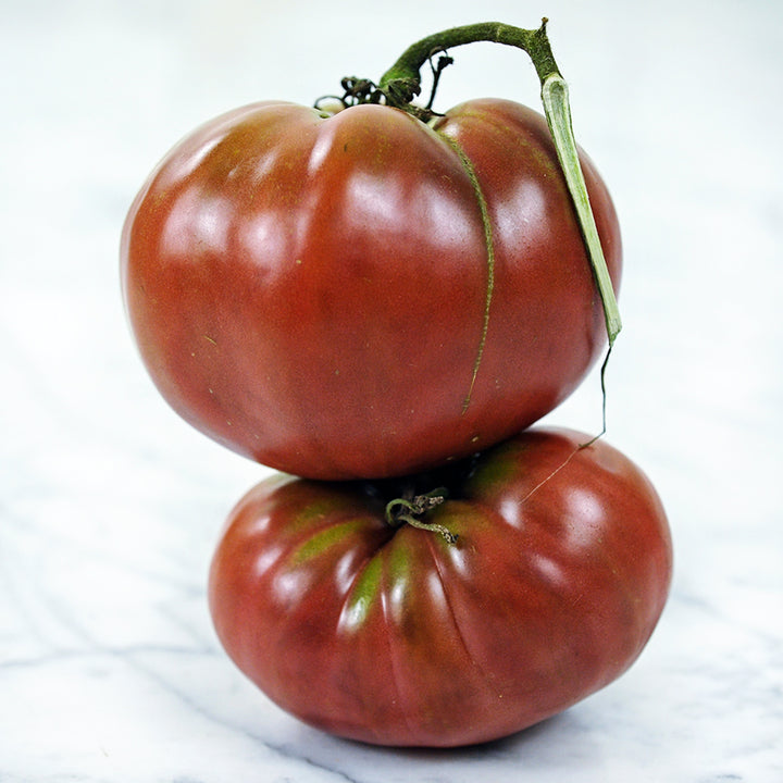Two True Beefsteak or Fejee Improved Tomatoes stacked on a white marble countertop.