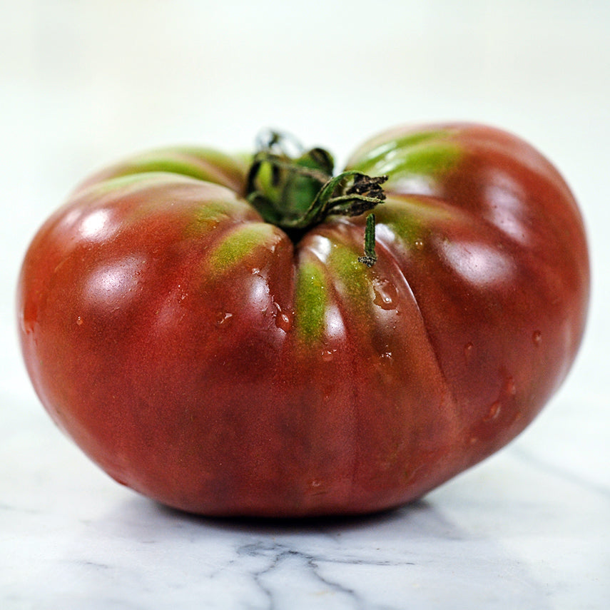 A side view of a single True Beefsteak or Fejee Improved Tomato on white marble countertop.