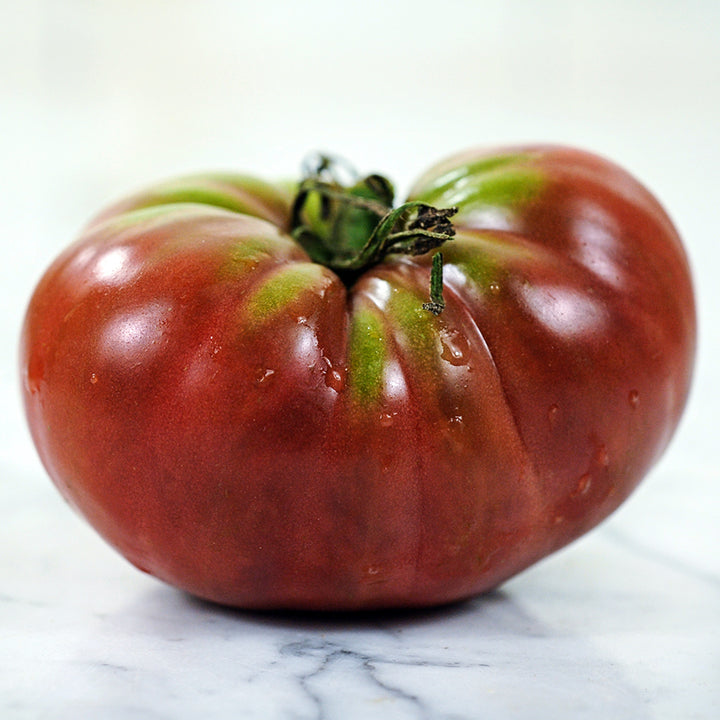 A side view of a single True Beefsteak or Fejee Improved Tomato on white marble countertop.