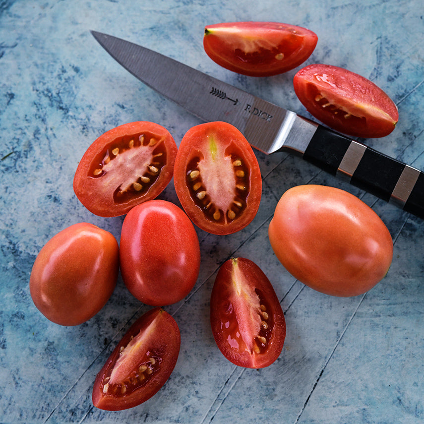 Cut and whole German Lunchbox Tomatoes with a German knife on variegated blue background.