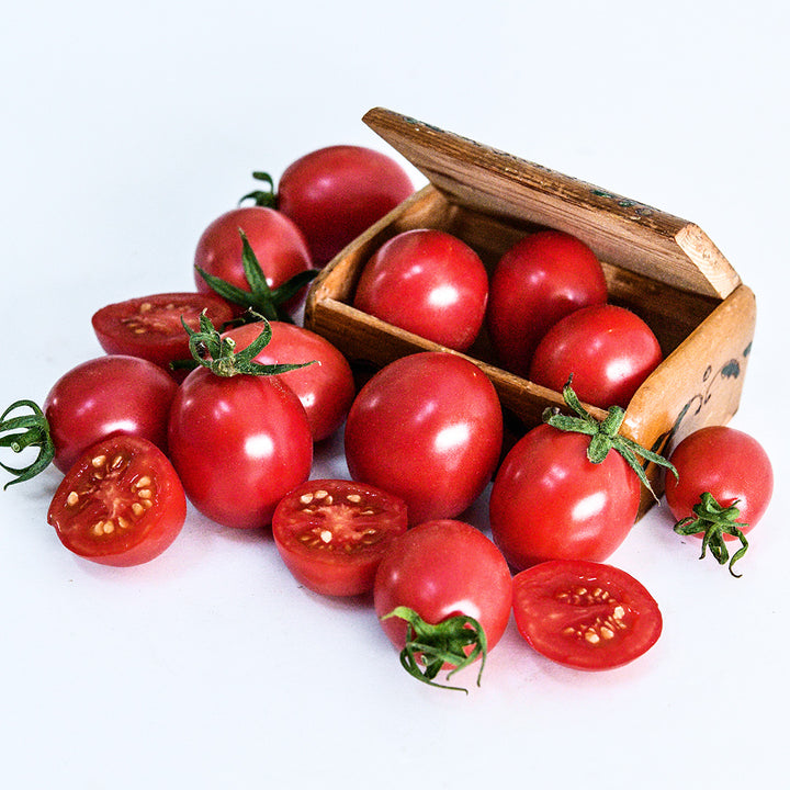 Cut and whole German Lunchbox Tomatoes in and surrounding a wooden box from Germany on white.
