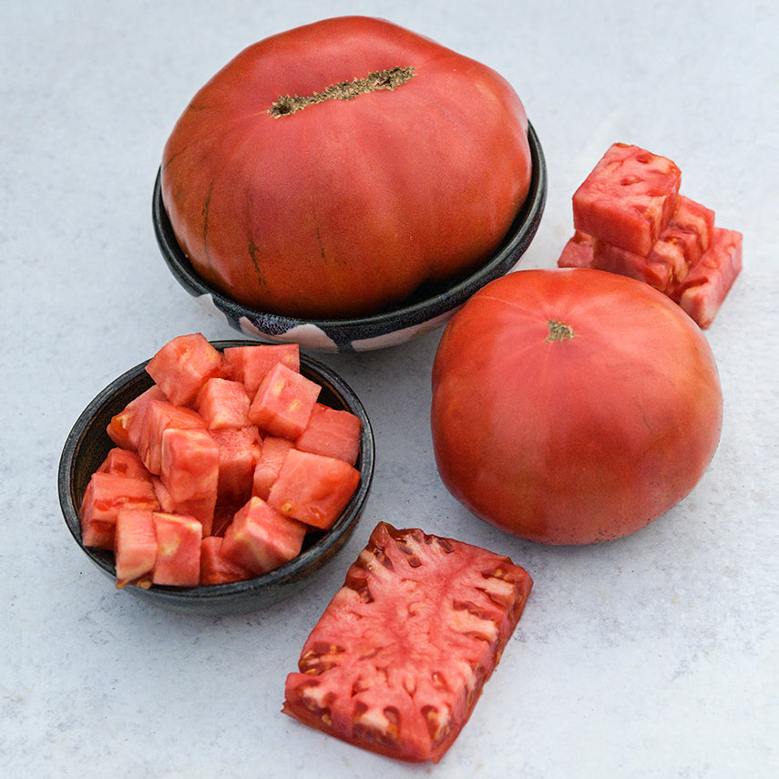 A couple of whole German Pink Tomatoes with chopped and cut tomatoes on light background.