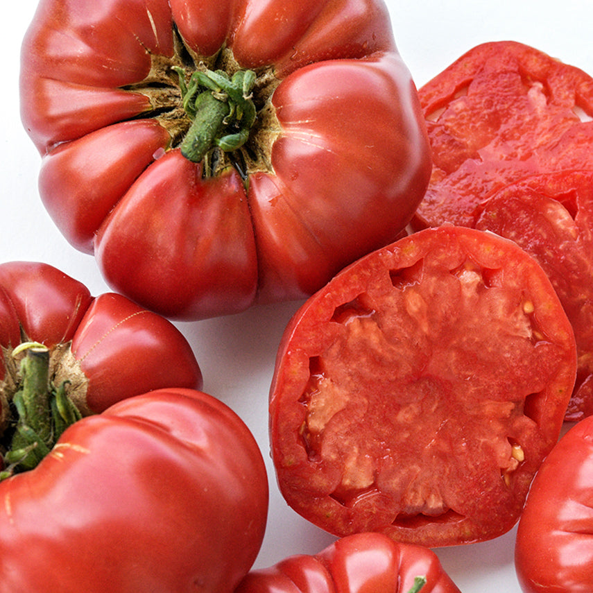 Close-up of cut and whole German Pink tomatoes on a white background.