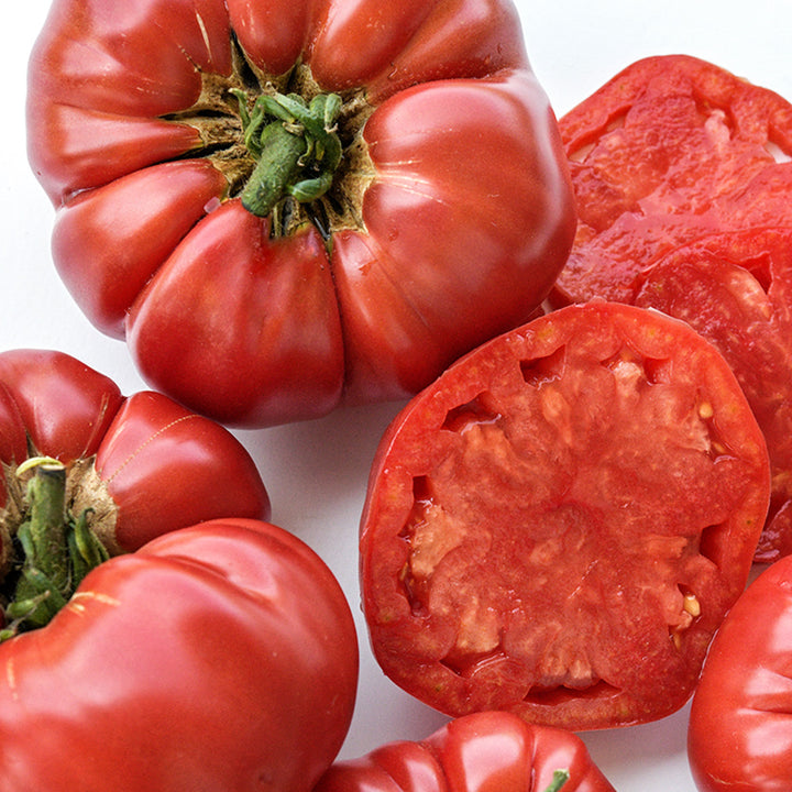 Close-up of cut and whole German Pink tomatoes on a white background.