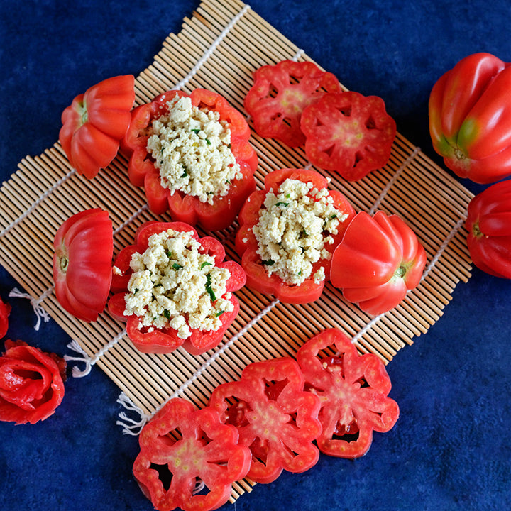 Stuffed Gezahnte Tomatoes with slices arranged on bamboo matt on a royal blue background.