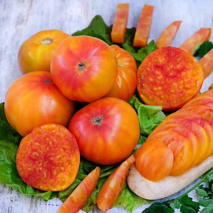 Cut, whole and sliced Gold Medal Tomatoes on a light wood background.
