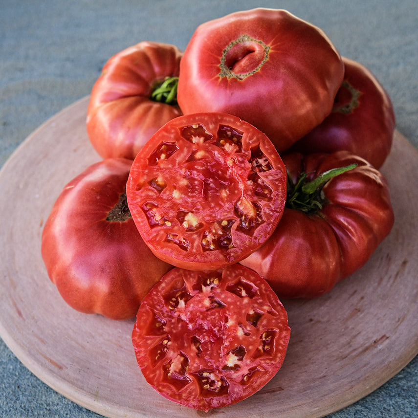 Cut and whole Granny Cantrell German Red Tomatoes on a terra-cotta red pizza stone.