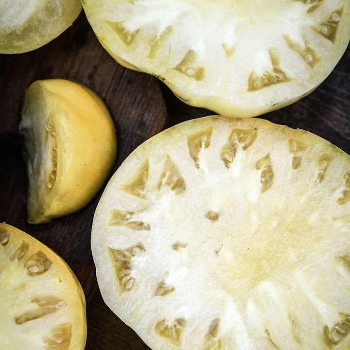 Close-up detailed view of slices of Great White Tomatoes on a wooden cutting board.