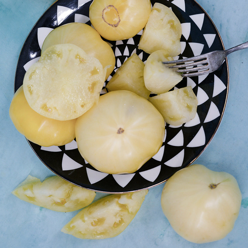 Sliced and whole Great White Tomatoes arranged on a black and white plate on a light blue background.