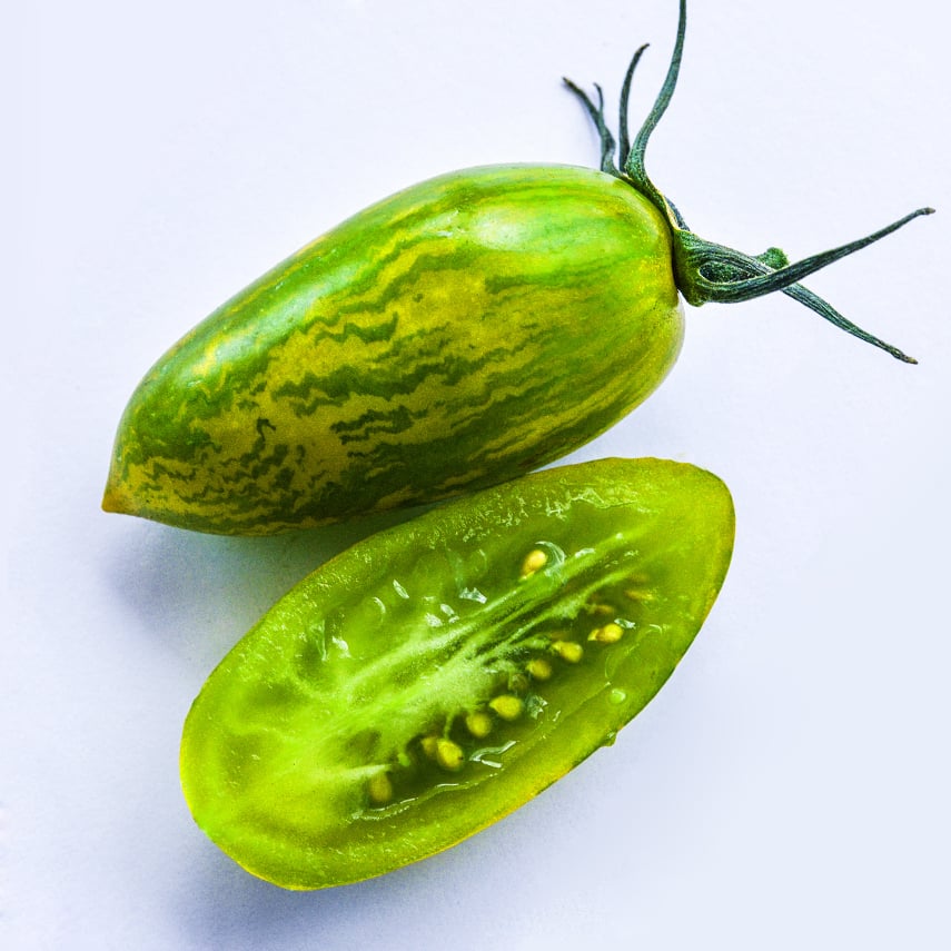 A macro close-up of a whole Green Tiger Tomato with a half slice on a white background.