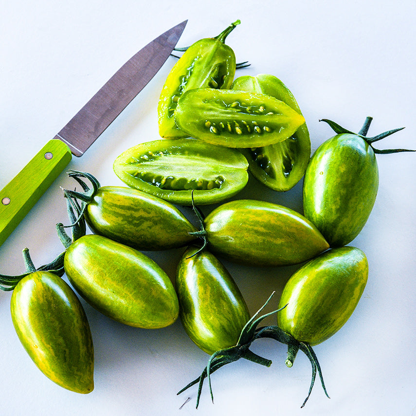 A bunch of sliced and whole Green Tiger Tomatoes with a green handled knife arranged on a white background.